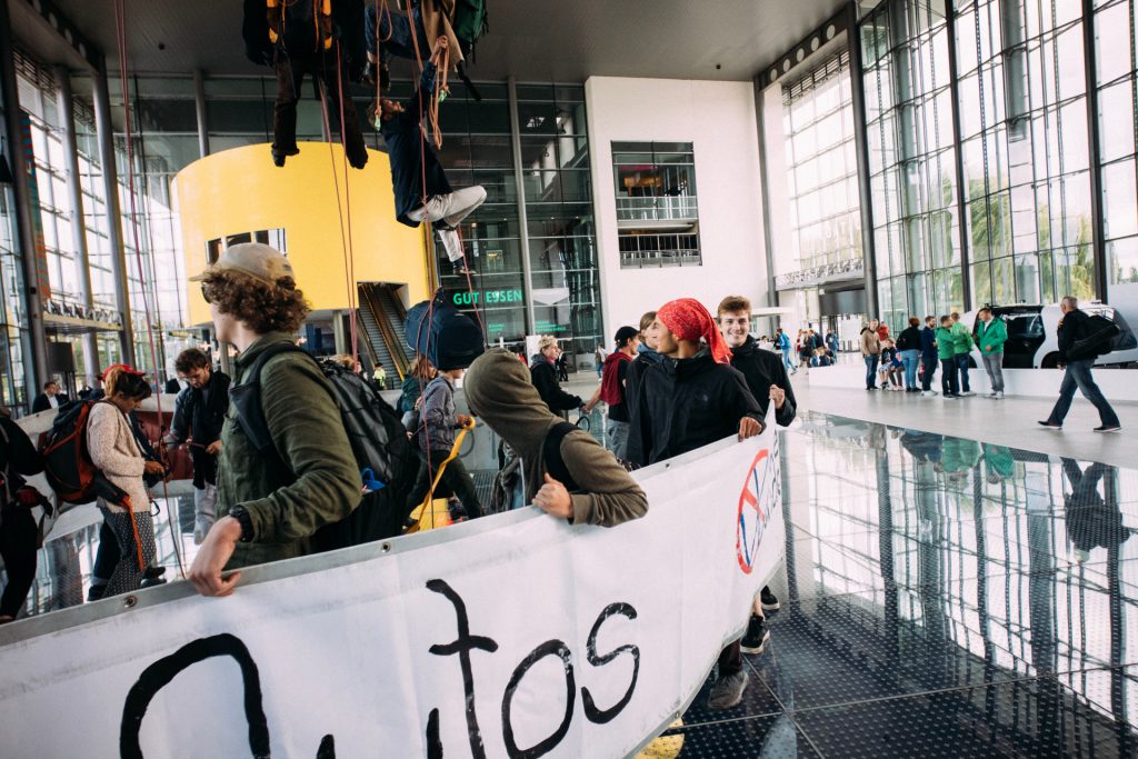 Aktivist*innen klettern zum Globus hoch, Demonstrant*innen schirmen sie ab.