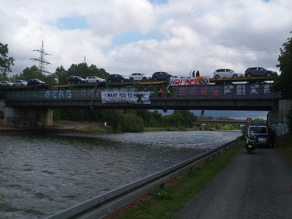 Aktivist*innen hängen von der Brücke herunter - auf ihrem Transpi steht "I want you to panic - abolish capitalism".