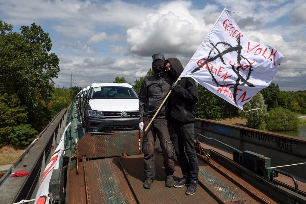 Zwei Aktivistis stehen auf dem Autozug. Auf ihrer Fahne steht "Gegen Volk und gegen Wagen".